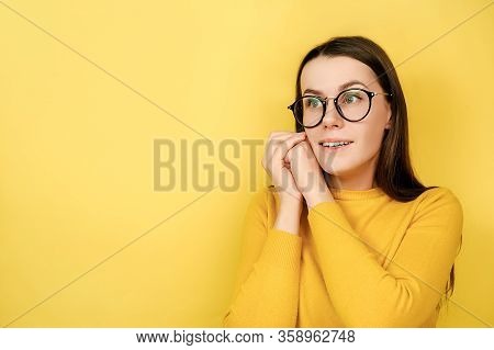 Portrait Of Optimistic Glad Young Woman In Eyeglasses With Cheerful Expression, Touches Cheeks, Look