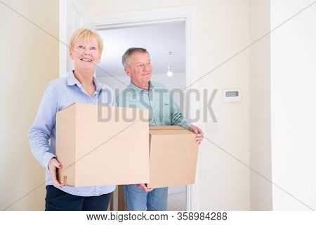 Senior Couple Downsizing In Retirement Carrying Boxes Into New Home On Moving Day