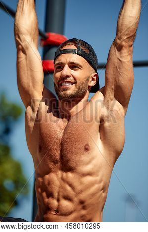 Athletic Sportsman Trains On The Horizontal Bars. Training At The Open Air Sprorts Ground.