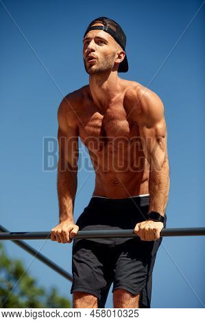 Athletic Sportsman Trains On The Horizontal Bars. Training At The Open Air Sprorts Ground.