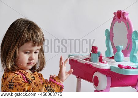 Little Cute Girl Is Trying To Wear Long Pink Necklace.