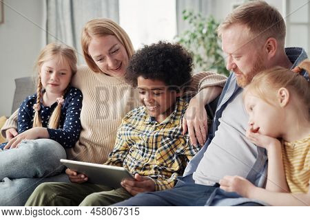 Happy Adopted Children Watching Video On Digital Tablet Together With Their Foster Parents During Le