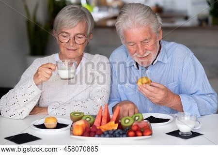 Beautiful Caucasian Retired Senior Couple Having Breakfast At Home With Fresh Seasonal Fruit, Milk A
