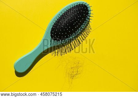 Green Comb And Fallen Hair On The Yellow Background. Baldness And Hair Loss Problem