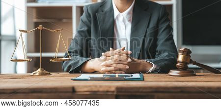 A Woman Lawyer Sits In The Office Of Her Law Firm, On A Table With A Scale Of Justice And A Hammer L
