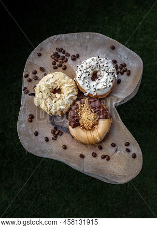 Three Doughnuts Covered With Cookies And Creme, Almendras And Choco Peanut Butter On Wooden Cutting 