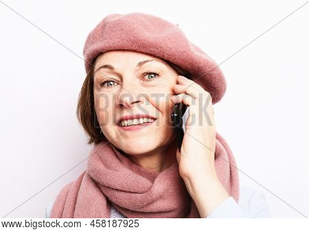 Elderly Woman Wearing Pink Scarf And Hat With Smartphone Over White Grey Background.