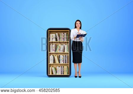 Young Woman Smiling And Take Note In Journal On Blue Background. Mobile Phone With Electronic Books 