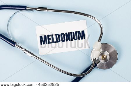 Stethoscope And White Card With Meldonium Text On Blue Background. Medical Concept.