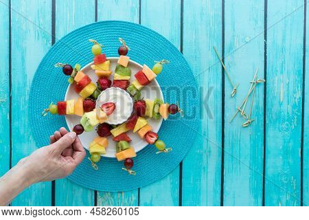 Top Down View Of A Platter Of Fresh Fruit Kebabs With Yogurt Dip In The Middle.
