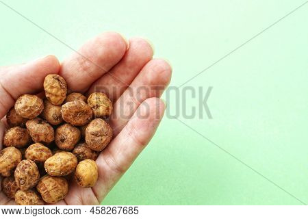 Chufa, Tigernut, Earth Almond In The Palm Of Outstretched Hand On Green Background. Healthy Vegan Fo