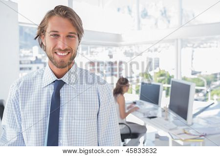 Sorrindo o coordenador de criação & pé no escritório com colelague trabalhando por trás