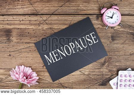 Menopause Word Written On Black Board, Flowers, Clock And Pills On Wooden Background. Women Health A