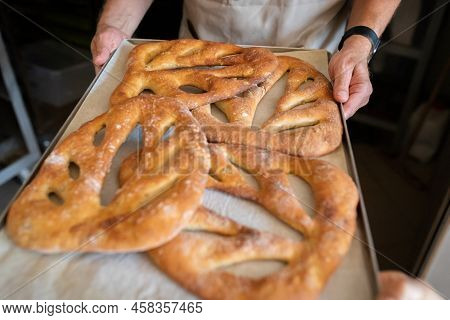 A Man In A Bakery Takes Traditional French Fougasse Bread Out Of The Oven. Front View.