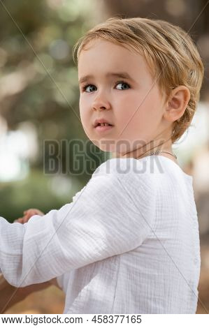 Portrait Of Toddler Girl In Shite Dress Looking Away Outdoors.