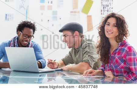 Team of editors at work with one smiling at camera in modern creative office