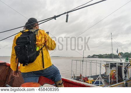 Latin Fisherman With Raincoat Checking The Weather Forecast On His Cell Phone On Top Of His Boat