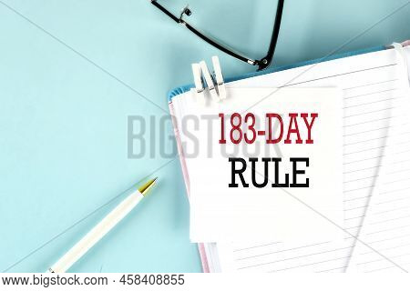 183 Day Rule Text On Sticky On A Notebook With Pen And Glasses , Blue Background