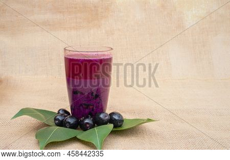 Closeup Of Jamun Or Syzygium Cumini Juice In A Glass With Fruit And Leaves Isolated On Burlap Fabric