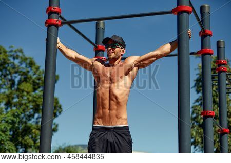 Athletic Sportsman Trains On The Horizontal Bars. Training At The Open Air Sprorts Ground.
