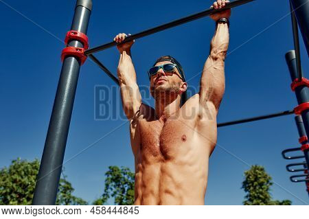 Athletic Sportsman Trains On The Horizontal Bars. Training At The Open Air Sprorts Ground.