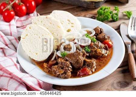 Pork Goulash Meat With Dumplings On White Plate, Cutlery, Garlic, Onion, Pepper, Tablecloth In The B