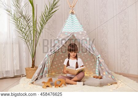 Full Length Portrait Of Little Girl With Braids Reading Book While Sitting In Children's Peetee Tent