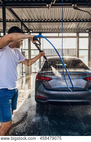 Self-service Car Wash. A Man Washes Off The Foam From His Car With Water From A Pressurized Hose At 
