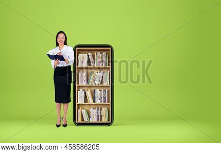 Young Woman Smiling And Take Note In Journal On Green Background. Phone With Electronic Books On Lar