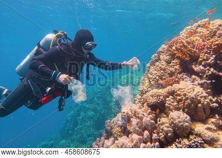 Man Scuba Diver Cleaning Plastic  From The Tropical Coral Reef. World Ocean Contaminated By Plastic.