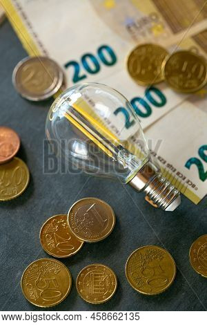 Electricity Cost. Light Bulb, Euro Banknotes And Coins On Black Chalk Board.increasing The Cost Of L
