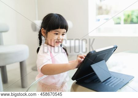 Asian Girl Looking And Touch On Tablet Screen Attentively. Overstimulated Children Concept. Too Much