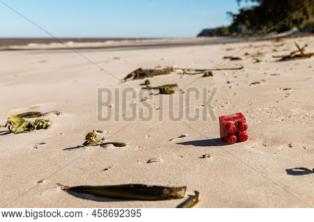 A Children\'s Toy For Construction By Blocks, Red In Color, Thrown In The Sand As Garbage And Pollut