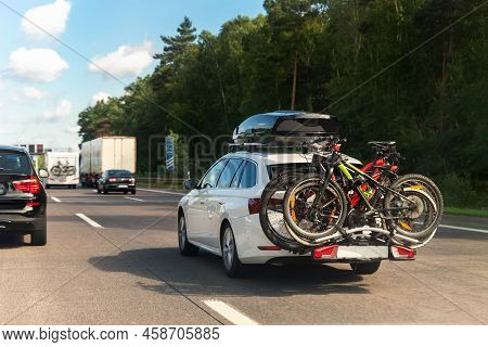 Back View Modern White Family Wagon Car With Mounted Roof Box Trunk And Bike Tail Carrier Driving Eu