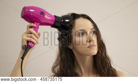 A Woman With Curly Hair Dries Her Hair With A Hair Dryer With A Diffuser Attachment.