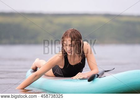 A Beautiful Girl Is Floating On A Supboard On A River. Young Woman Supsurfing At Sunrise.