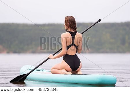 A Beautiful Girl Is Floating On A Supboard On A River. Young Woman Supsurfing At Sunrise.