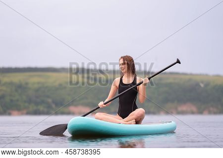 A Beautiful Girl Is Floating On A Supboard On A River. Young Woman Supsurfing At Sunrise.