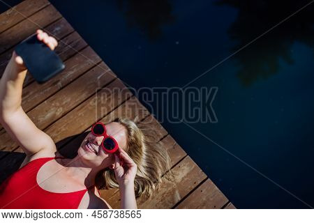 Rlaxed Woman Wearing Headphones Listening To Music And Taking Selfie When Lying On A Pier By Natural