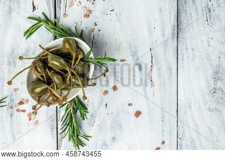 Capers. Marinated Or Pickled Canned Capers Fruit With Fresh Rosemary In A Small Bowl, On Gray Backgr