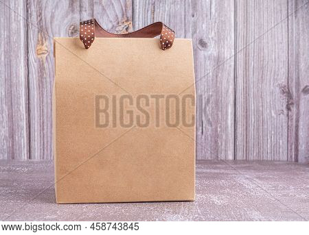 Brown Paper Bag Packaging With Ribbon Handles Placed On A Gray Stone Background With A Wooden Wall. 