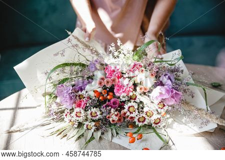 A Woman Florist Packs A Multi-branch Bouquet In White Paper On The Table In Her Flower Studio. Only 