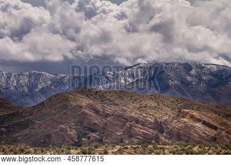 Vasquez Rocks In The Foreground With Mountains And Fresh Snow In The Distance Under Dramatic Clouds
