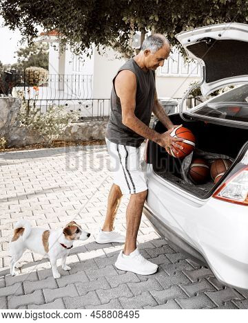Basketball Coach Puts The Balls Into The Trunk Of His Car Going To Workout. A Cute Dog Jack Russell