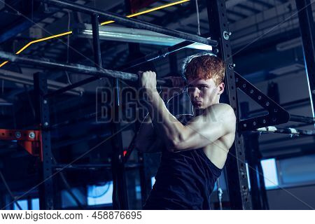 Portrait Of Sportive Muscular Young Man Training, Doing Pull Up Exrcises Isolated Over Gym Backgroun