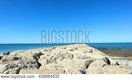 Breakwater A Pier Made Of Large Old Stones Leading Far Into The Sea. Far Perspective, Road Across Th