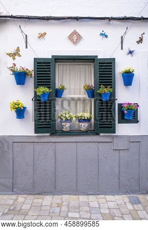 A White Facade With A Window Of A Typical Mediterranean House With Blue Pots With Colorful Flowers A