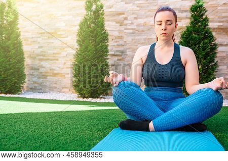 Young Redheaded Fitness Woman Practising Meditation Outdoors, In The Garden Of Her House, Doing Yoga