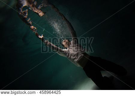 Underwater Shooting With Contrasting Light, A Guy Is Swimming Underwater, Pulling His Hand To His Re
