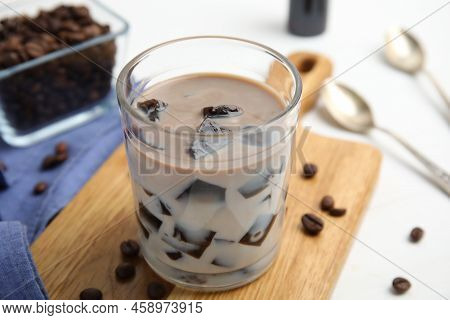 Glass Of Milk With Grass Jelly And Coffee Beans On White Table, Closeup